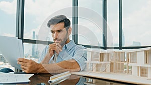Architect engineer checking house model while holding blueprint. Disputation