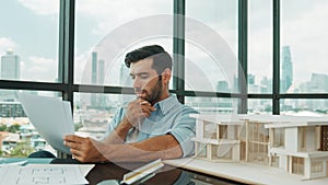 Architect engineer checking house model while holding blueprint. Disputation