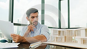 Architect engineer checking house model while holding blueprint. Disputation