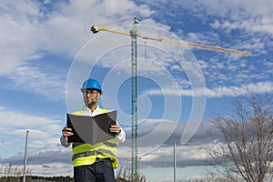 Architect or Engineer holding documents on the construction site. Job concept. Wearing protective clothes. Crane on the background