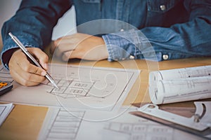 Architect or engineer holding pen pointing construction project equipment on the desk with a blueprint in the office