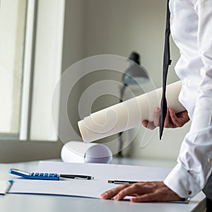 Architect or engineer leaning on his office desk holding rolled