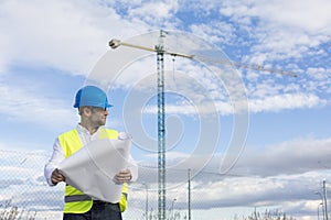 Architect or Engineer man holding blueprints on the Construction Site. Wearing protection clothes. Crane on background over blue