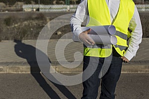 Architect or Engineer man holding blueprints on the Construction Site. Wearing protection clothes. Crane on background over blue