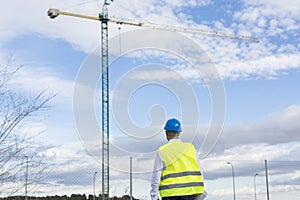 Architect or Engineer man holding blueprints on the Construction Site. Wearing protection clothes. Crane on background over blue