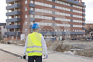 Architect or Engineer man holding blueprints and tablet on the Construction Site. Wearing protection clothes. Crane on background