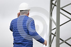 Architect or engineer talking on smart phone in front of a power pole