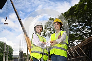 Architect and engineer wearing safety helmet and yellow vests standing at construction site with beautiful clouds and