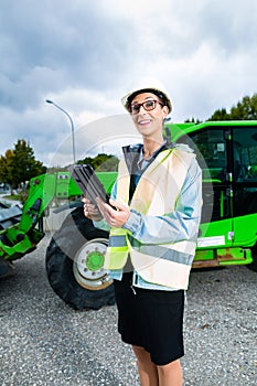 Architect in front of excavator using pad or tablet