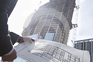 Architect holding blueprint of building at a construction site, midsection photo