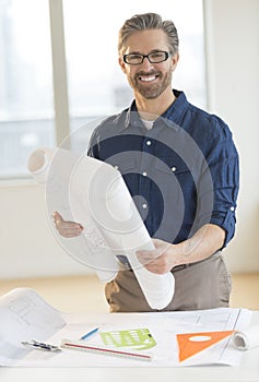 Architect Holding Blueprint At Desk In Office