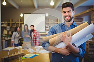 Architect holding blueprints while standing in creative office