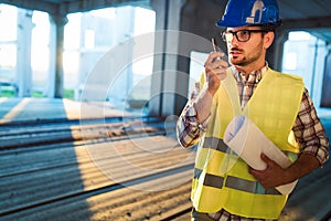 Architect holding rolled up blueprints at construction site