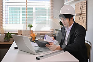 Architect male using digital tablet and working on architectural plan at office.