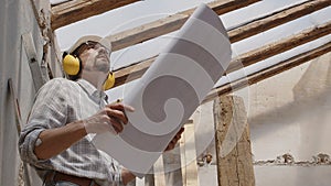 Architect man at work, wearing helmet and headphones looking at blueprint , check the construction house project plan, in