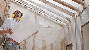 Architect man at work, wearing helmet and headphones looking at blueprint , check the construction house project plan, in