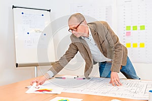 Architect Reaching For Document While Working On Blueprint