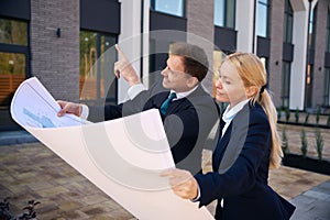 Architect showing house to client while standing with opened plan