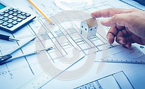 Architect with small house model on hand and plan design.Concepts of architecture,construction,engineering.