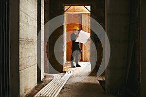Architect standing in house under construction with building plan