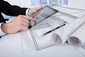 Architect using digital tablet on blueprint in office