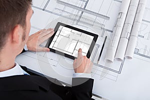 Architect using digital tablet on blueprint in office