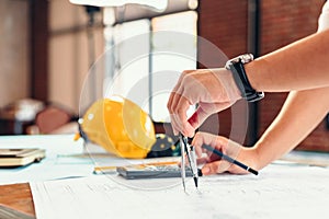 Architect using divider compass working on blueprint. blueprints, ruler, calculator, safety hat and book on the table.