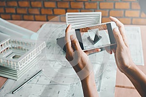 Architect using smart phone photograph model building in office.