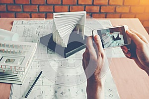 Architect using smart phone photograph model building in office.