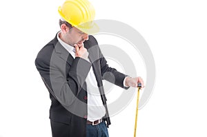 Architect wearing hardhat holding measuring tape and thinking