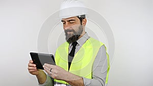 Architect wearing hardhat, isolated on white background standing with smile on face holding tablet.