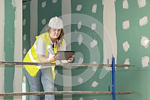 Architect wearing white helmet and a safety jacket leaning against a scaffolding and checking out the floor plans