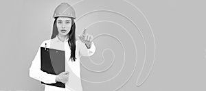 Architect woman in helmet pointing on copy space. Young woman in helmet hold clipboard on gray background. Woman