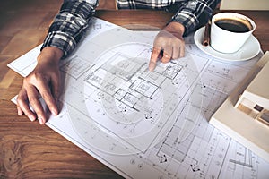 Architect working on an architecture model with shop drawing paper and coffee cup on table