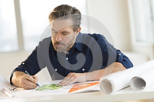 Architect Working On Blueprint At Desk