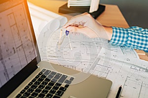 Architect working on blueprint in workplace with laptop and draw