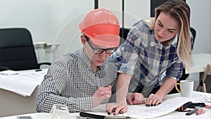 Architect working on blueprints while female colleague bringing more drawings