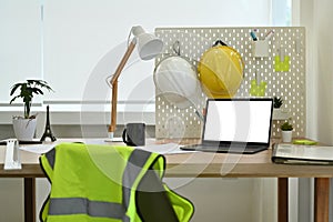 Architect working desk with laptop computer, hardhat, reflective jacket and stationery
