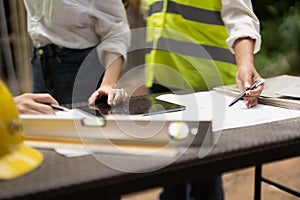 architector and engineers with draft plan of building and tablet computer talking on constructing site.