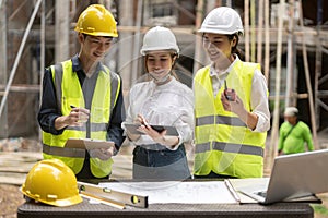 architector and engineers with draft plan of building and tablet computer talking on constructing site.