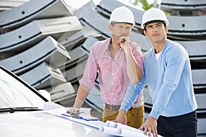 Architects with blueprints on car inspecting site