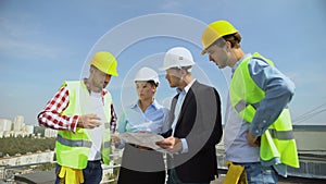 Architects discussing building plan with construction workers standing roof