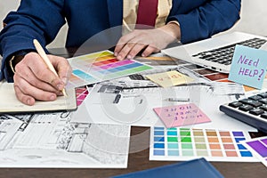 Architects hands drawing of modern apartaments with colour sample and laptop on creative desk, office. Man choosing colors for