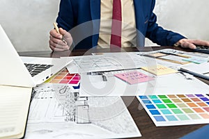 Architects hands drawing of modern apartaments with colour sample and laptop on creative desk, office. Man choosing colors for