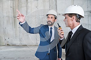 Architects in hardhats using walkie-talkie and discussing project at construction site