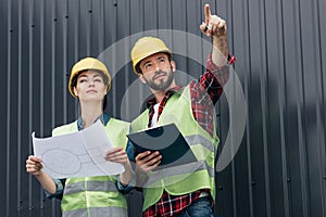 architects in helmets pointing and working with blueprint and clipboard