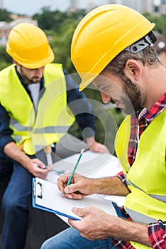 architects in safety vests and hardhats one of them writing