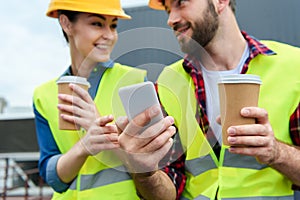 architects in safety vests and helmets using smartphone on coffee break