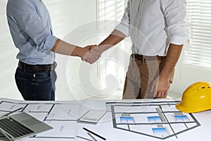 Architects shaking hands near table with construction projects in office, closeup