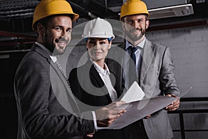 architects in suits and helmets working with blueprint and digital tablet